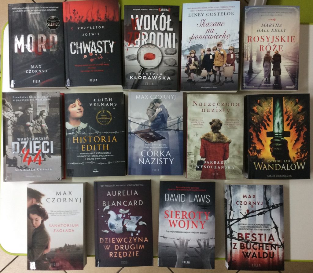 Ułożone w trzech rzędach książki. Okładki książek opisane nazwiskiem autora i tytułem.